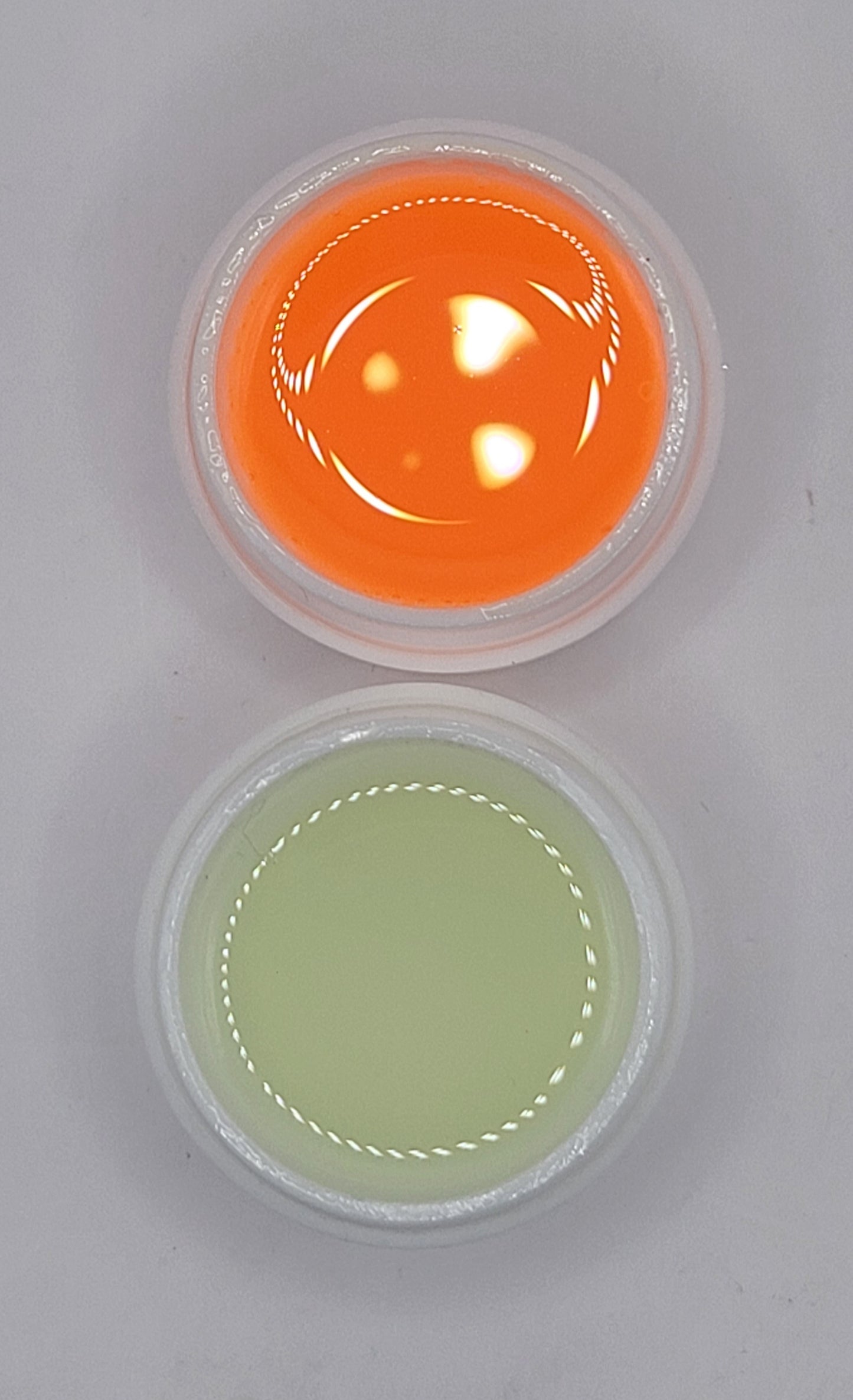 Two small containers with orange and green uv glow in the dark gel on a gray background