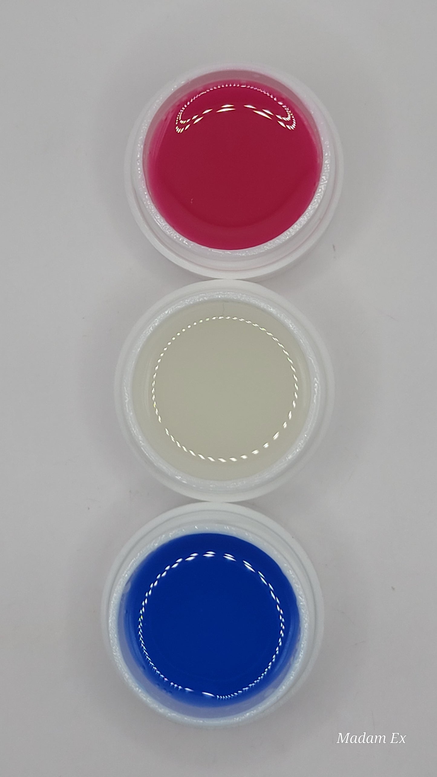 Three small containers with pink, white, and blue glow in the dark hard gel on a gray background