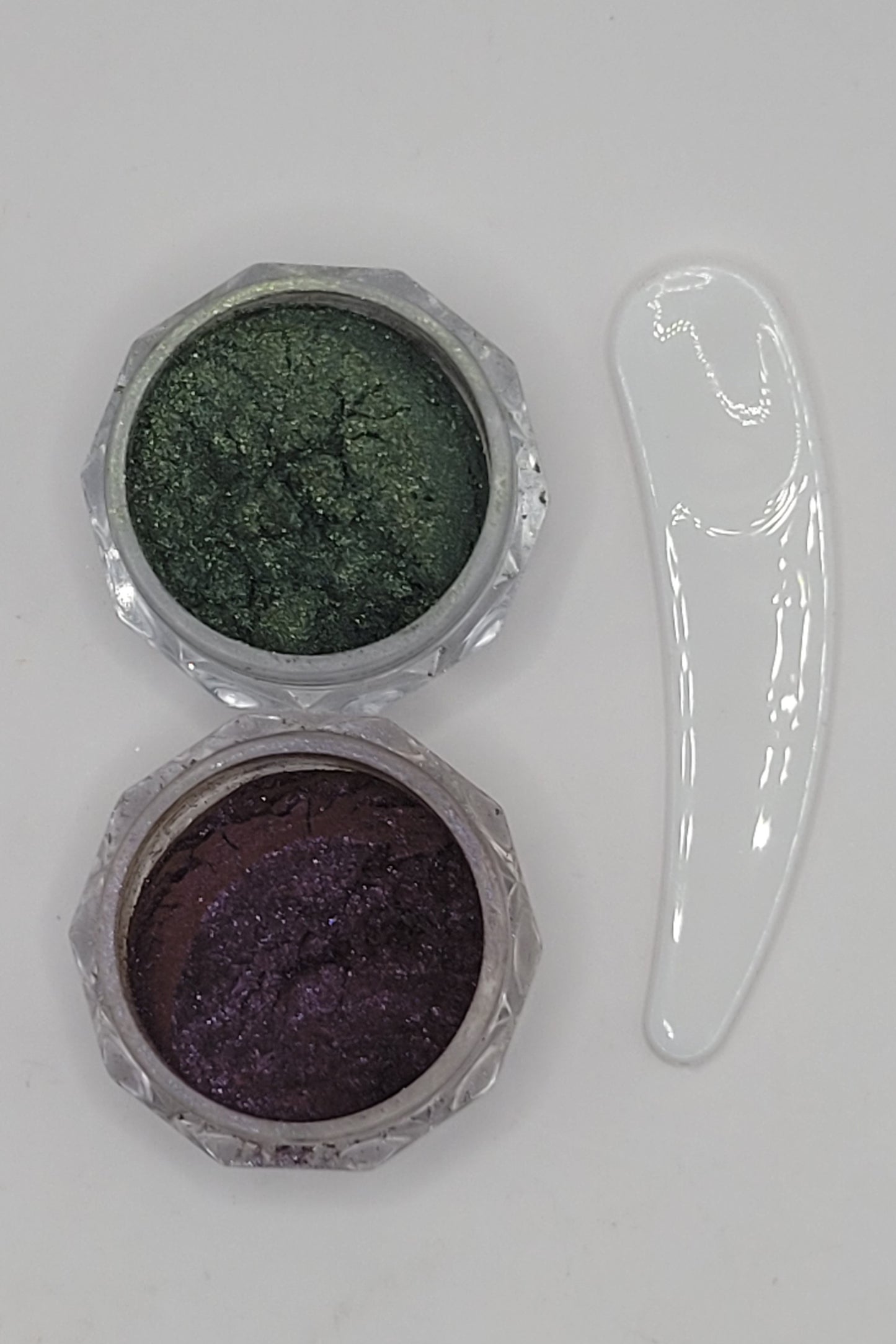 two small containers with cat-eye chameleon powder mix in a clear plastic containers on a white background green and plum