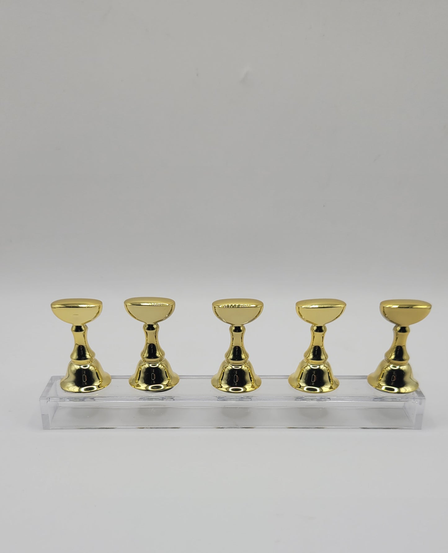 1 Set of five gold nail display stand on a clear stand against a gray background