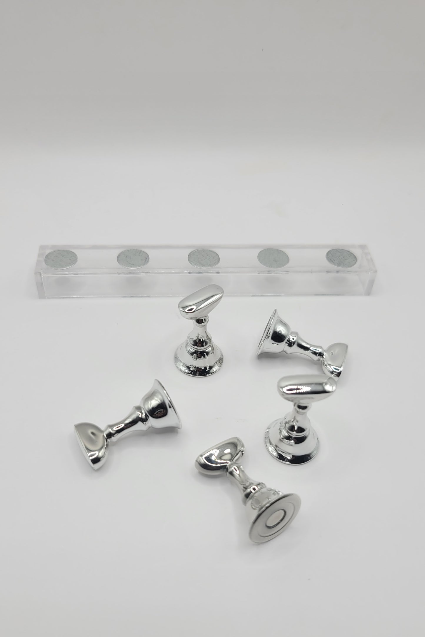 1 Set of five silver nail display pieces laying next to clear stand on against a gray background