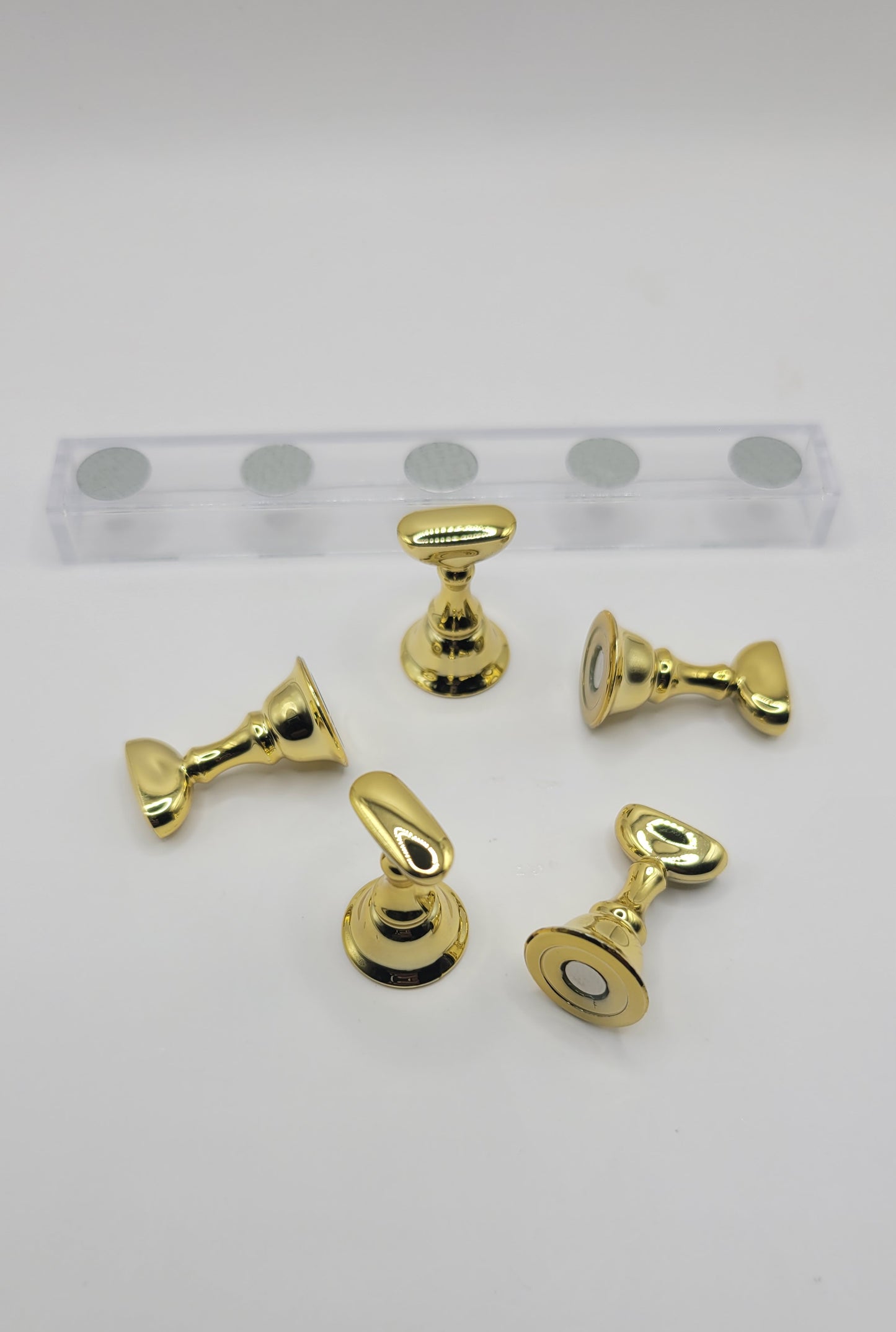 1 Set of five gold nail display pieces laying next to clear stand on against a gray background