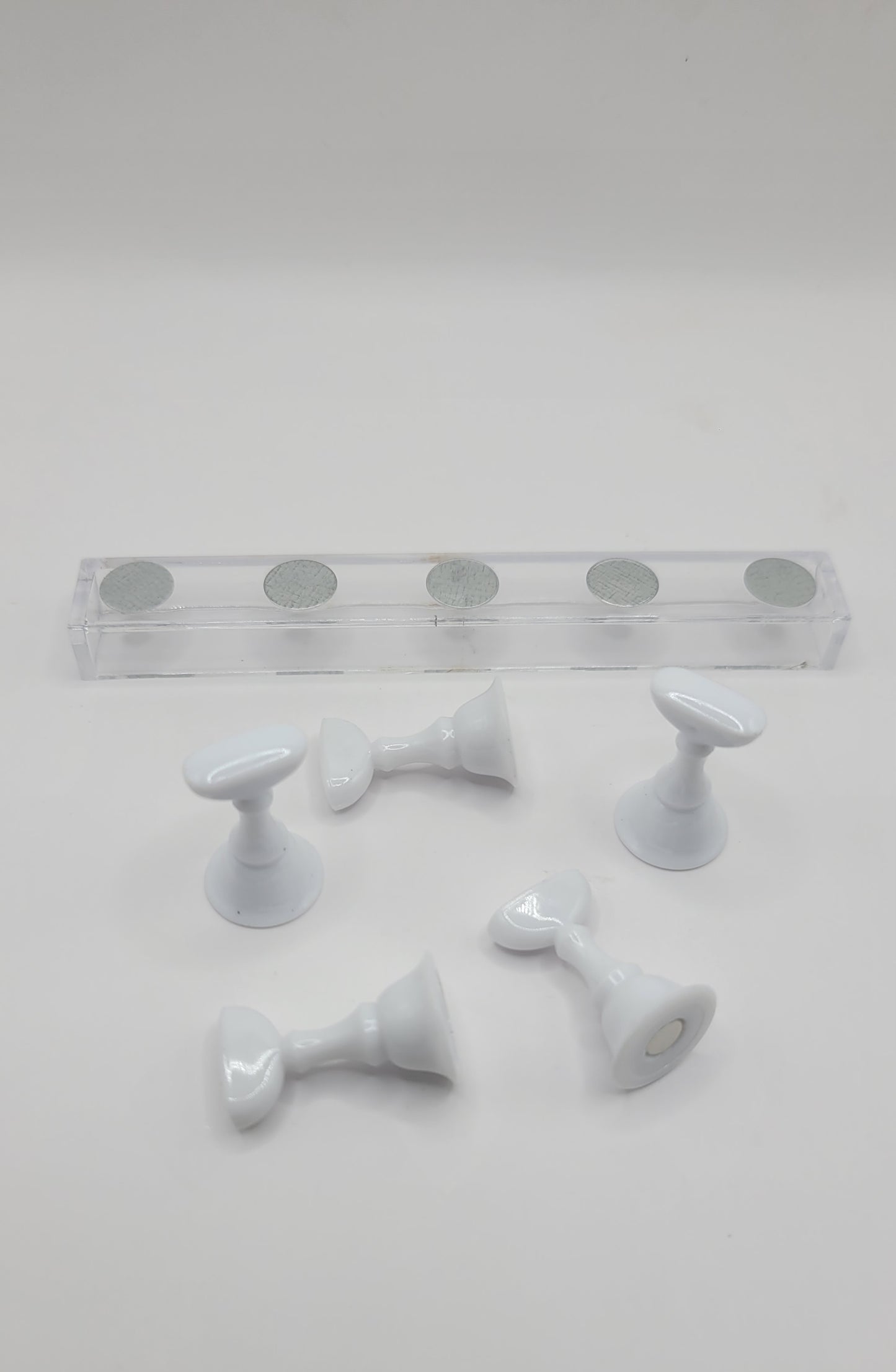 1 Set of five white nail display pieces laying next to clear stand on against a gray background