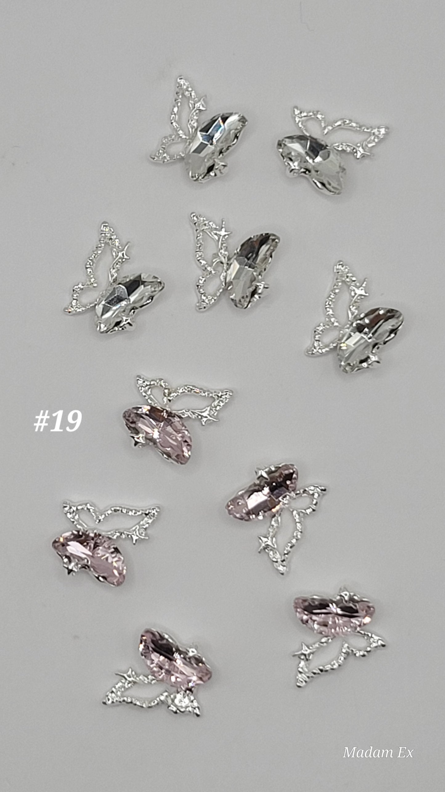 10 Butterfly-shaped decorative nail charms with pink and clear gemstones on a gray backgrounds