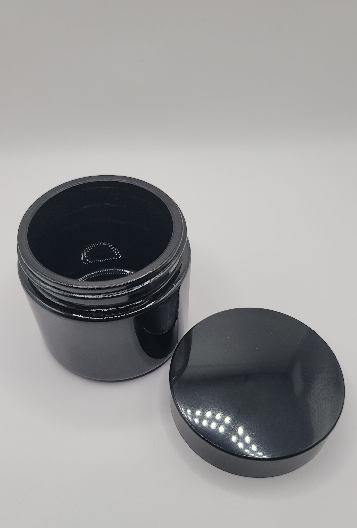 Black plastic jar with lid off next to it on a white background