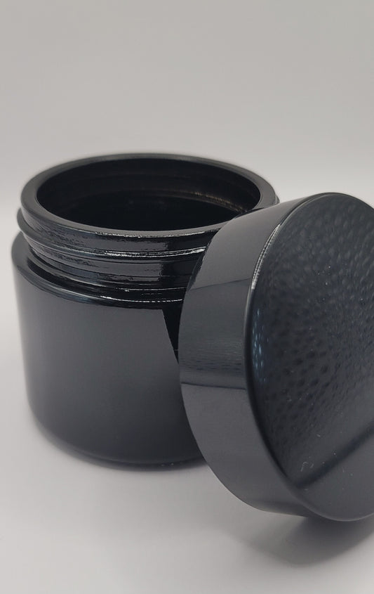 Black cosmetic jar with lid off leaning next to it on a light gray background