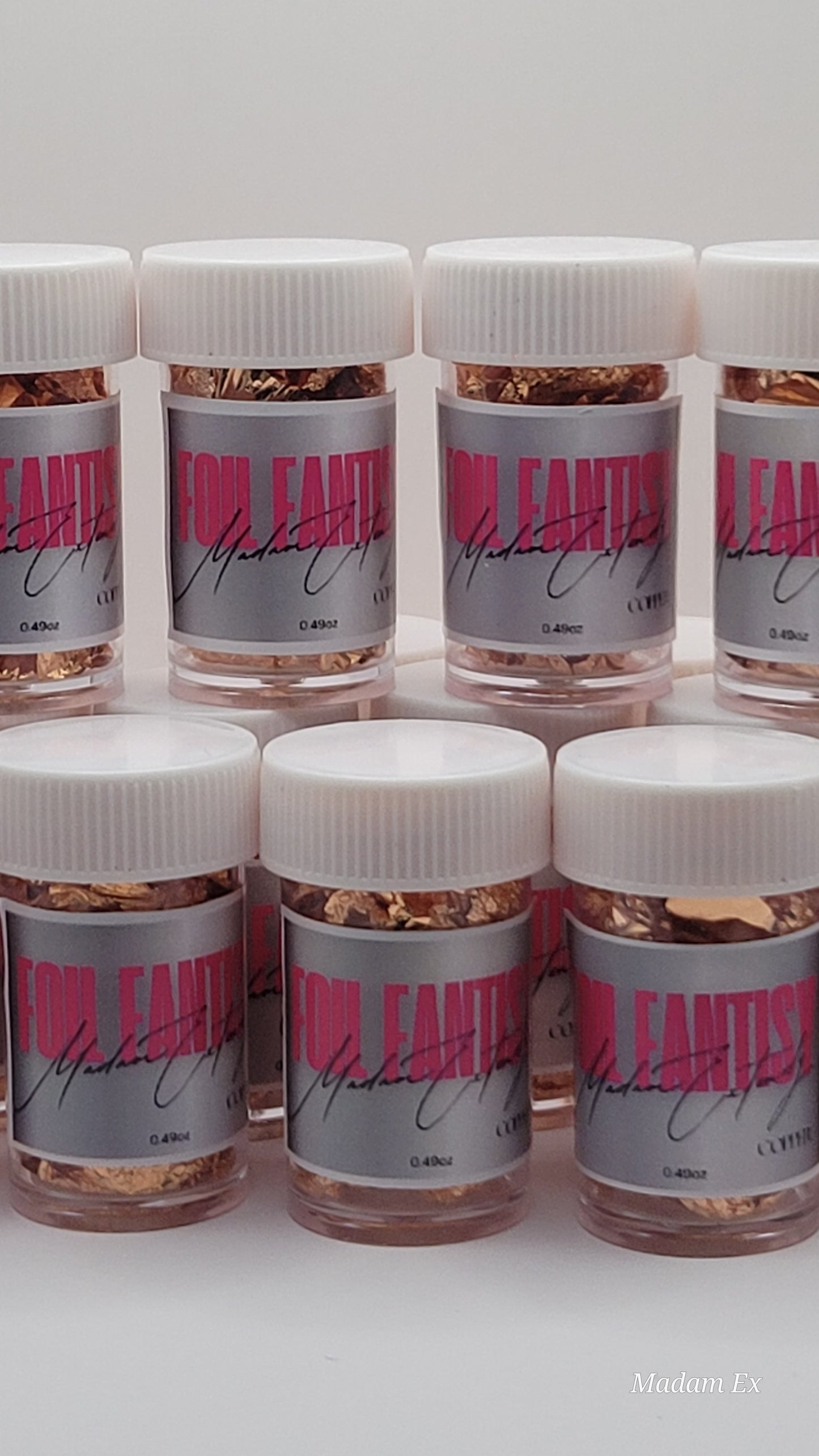 Multiple small jars of foil fantasy with white lids and pink labels on a white background