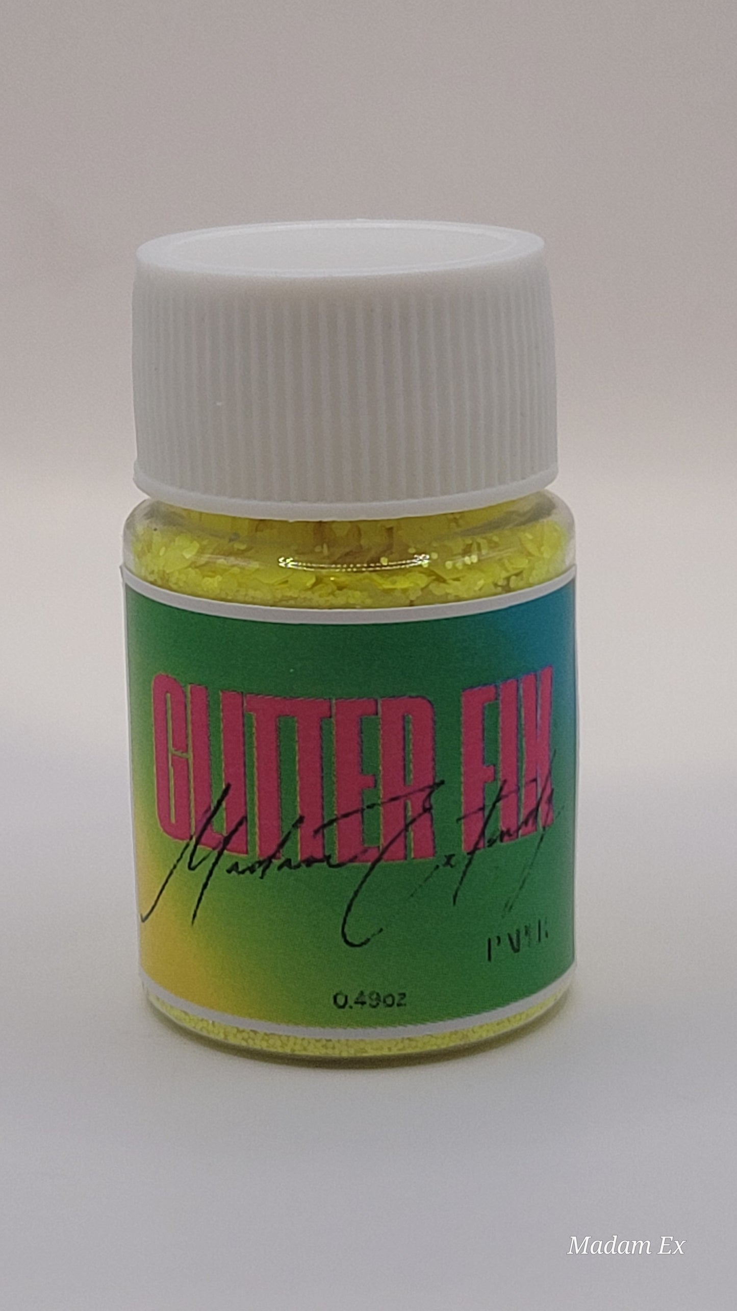Bottle of yellow Glitter Fix with green label and pink contents on a white background