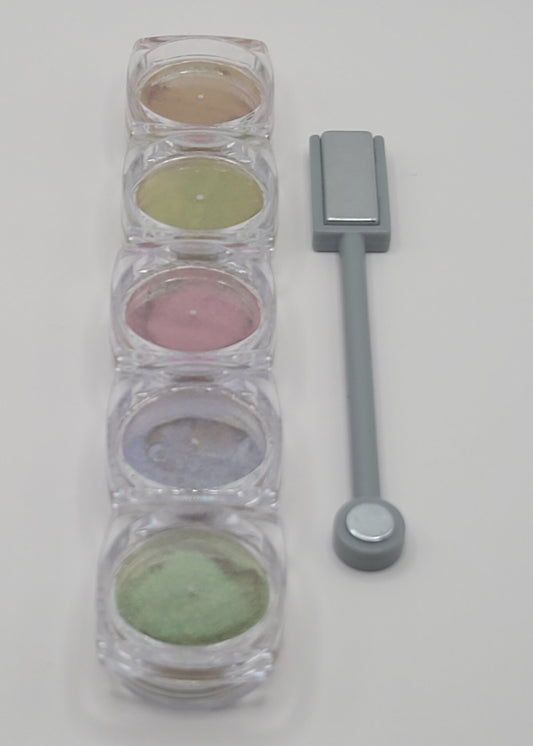 five small round containers with colorful cat-eye powder in a line with a cat-eye magnet on a white background