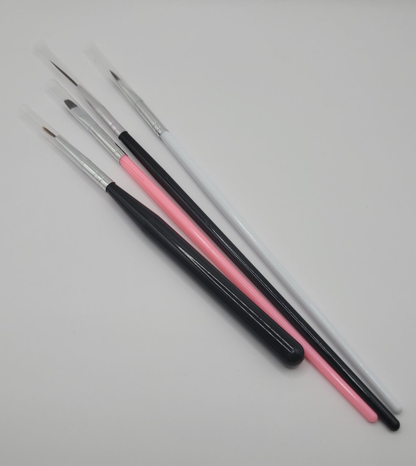 four piece 2 black and silver, 1 pink, 1 white nail art brushes on white background