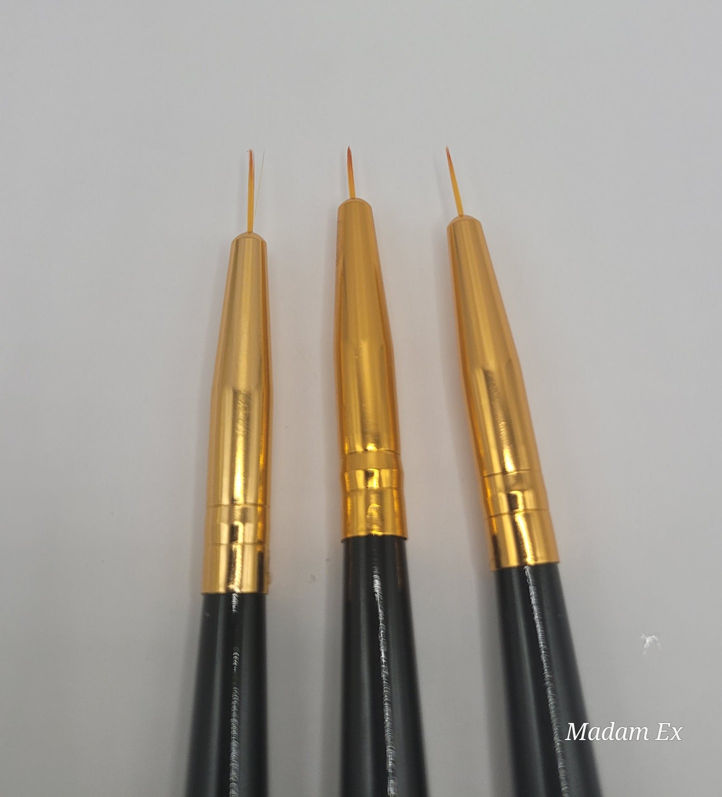 close-up view of three dual end black and gold nail art brush on white background