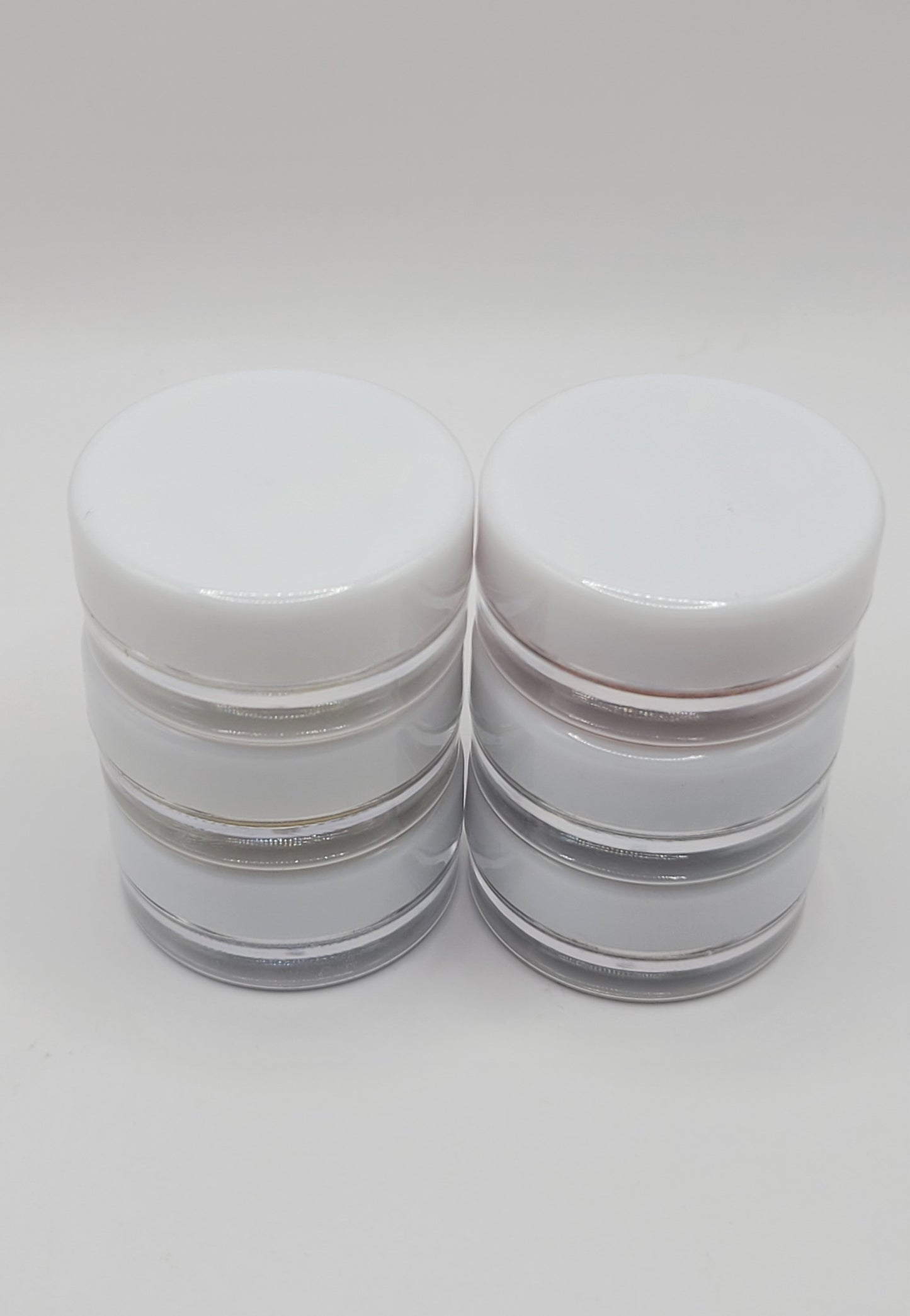 six cosmetic jars with white lids stacked in two sets on a light gray background