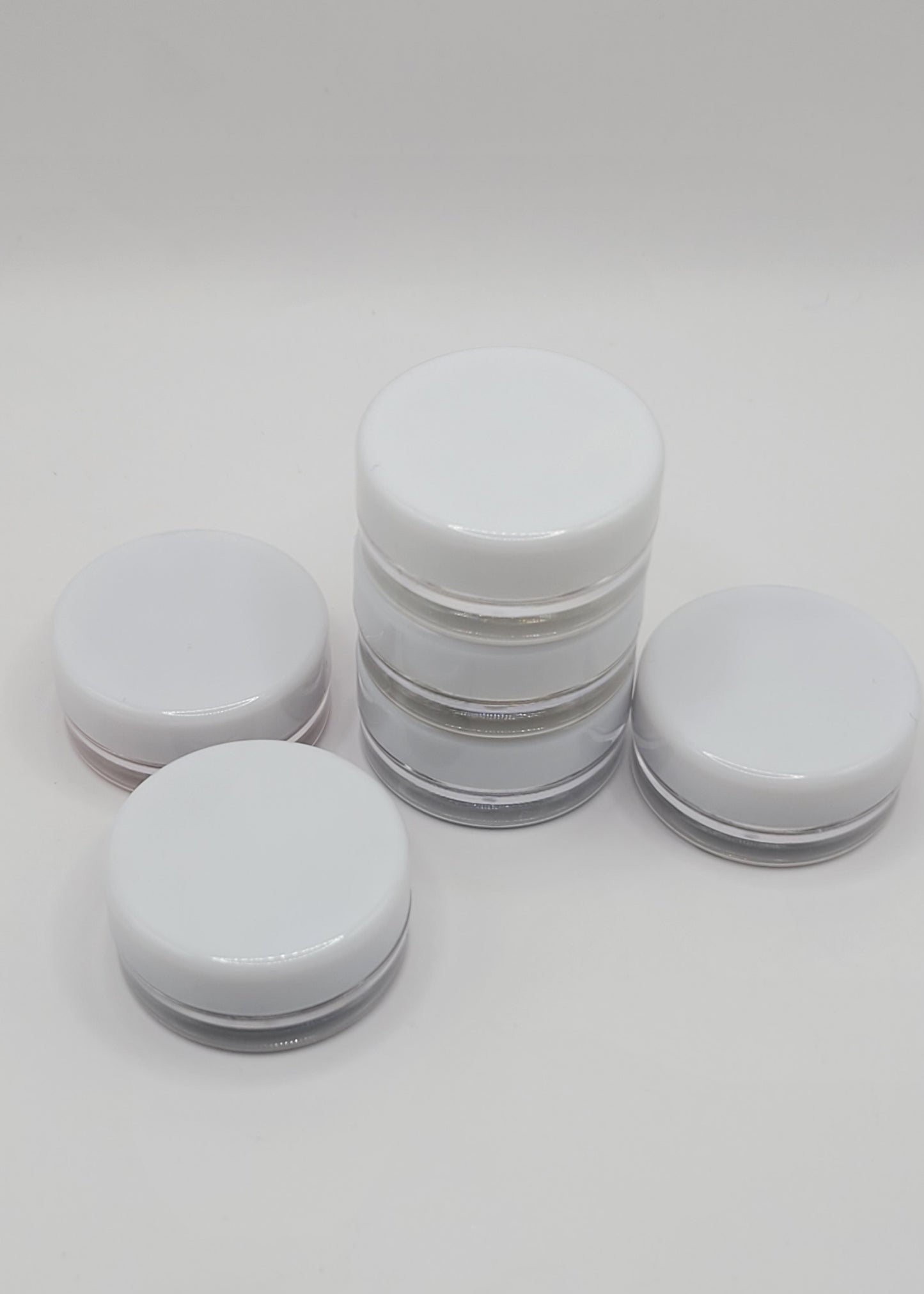 Set of 6 white jars one stack of 3 and the other surounding it sealed on a light gray background