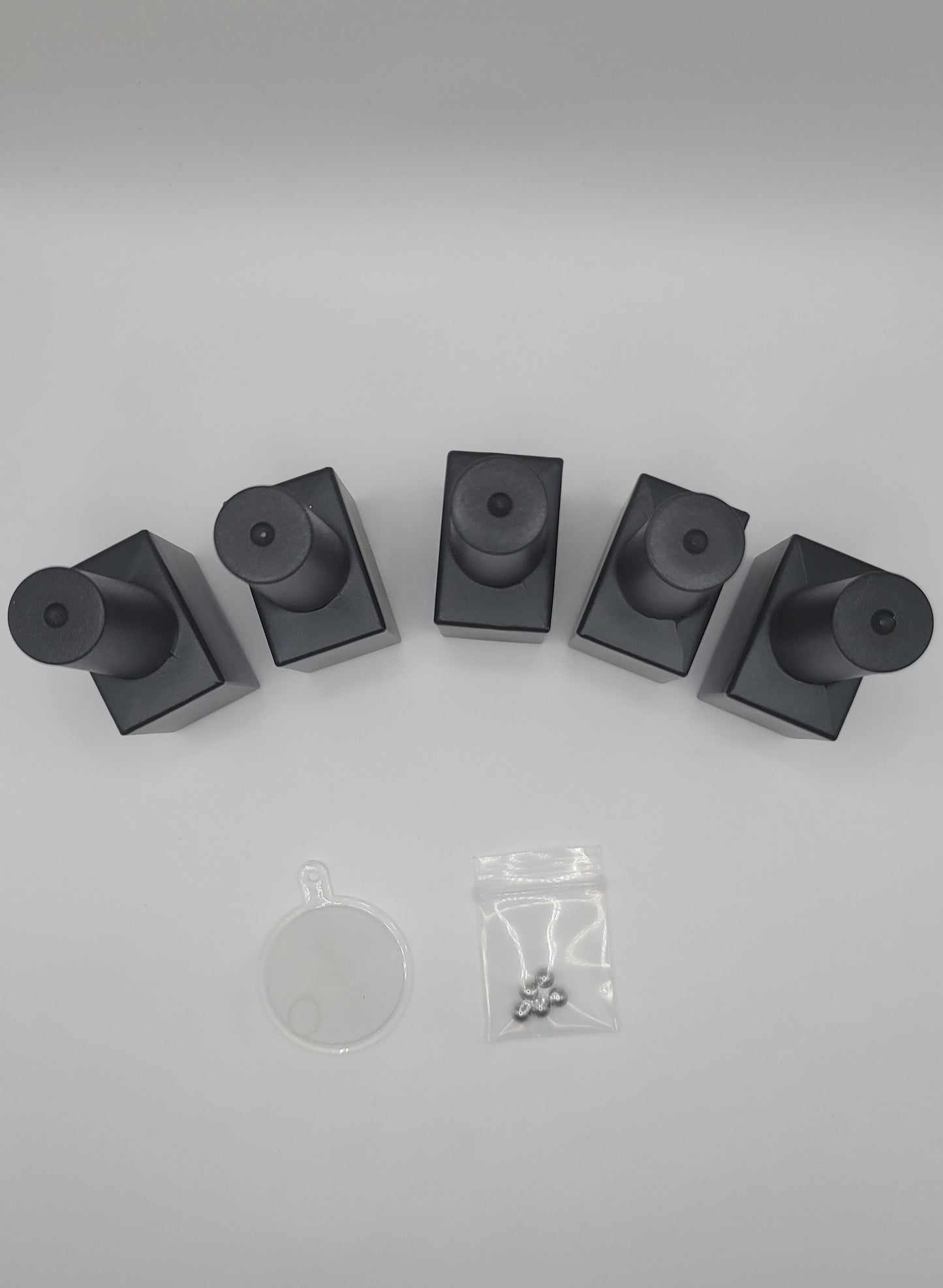Five black glass nail polish bottles top view and a small clear funnel with stiring beads on a white background