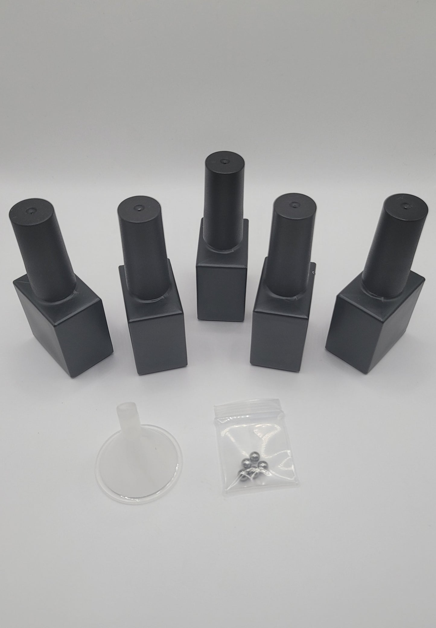5 Sets of black glass nail polish bottles on a white background with a clear plastic funnel and stiring beads