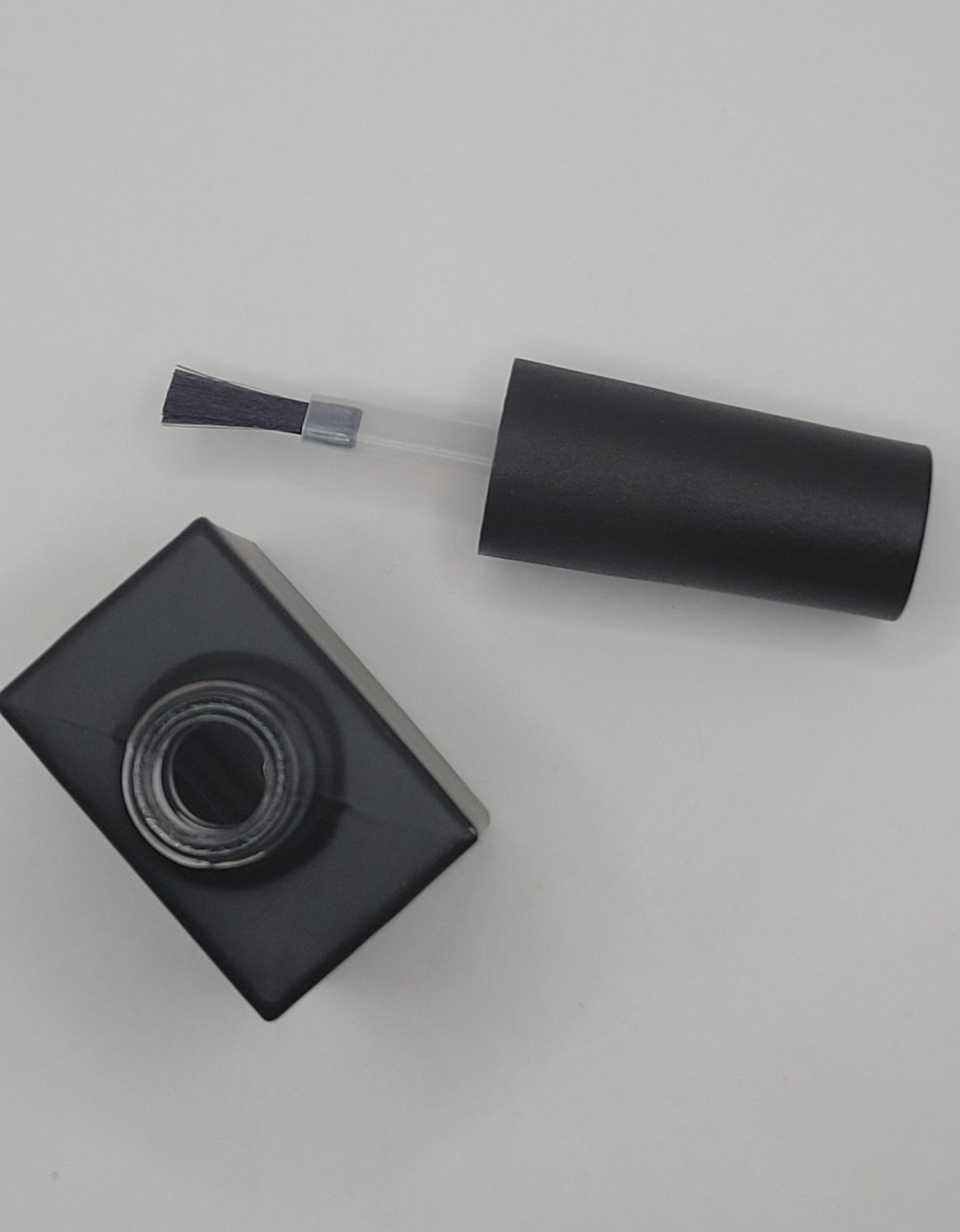 black cylindrical polish brush laying next to polish bottle on a light gray backgroundng