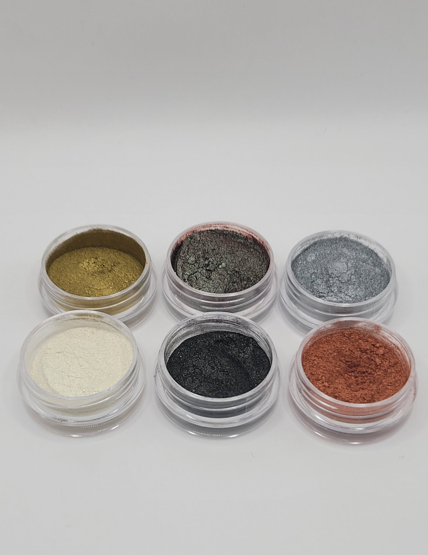 Set of six small round containers with metallic mica powders with tops off on a white background