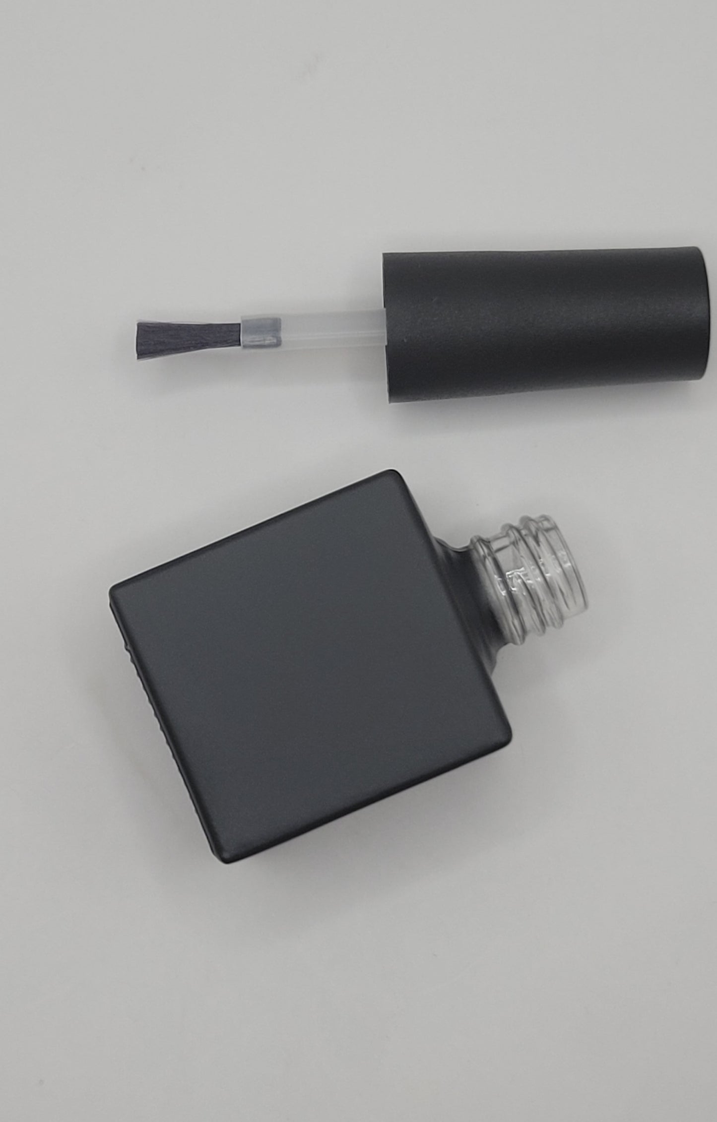 Black nail polish bottle with brush on a light gray background