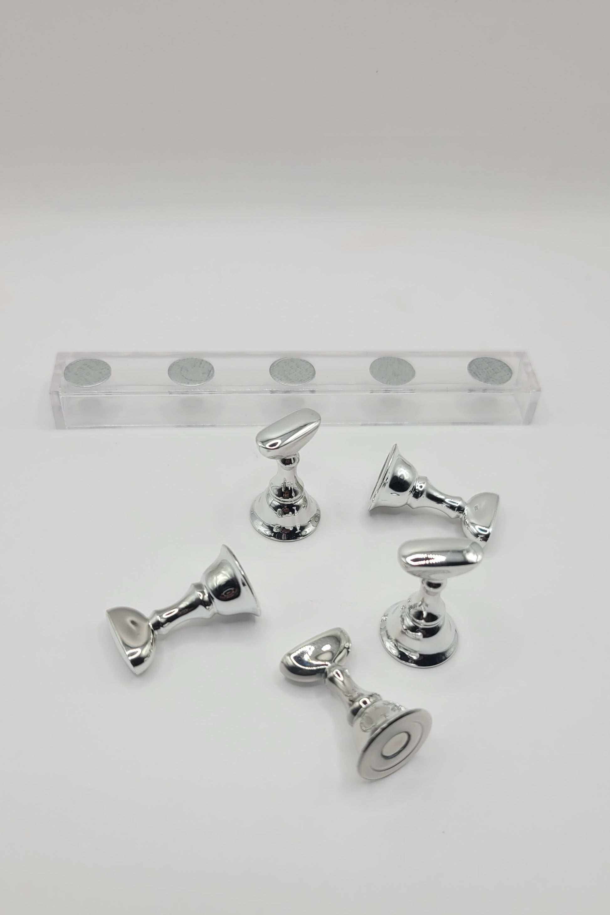1 Set of five silver nail display pieces laying next to clear stand on  against a gray background
