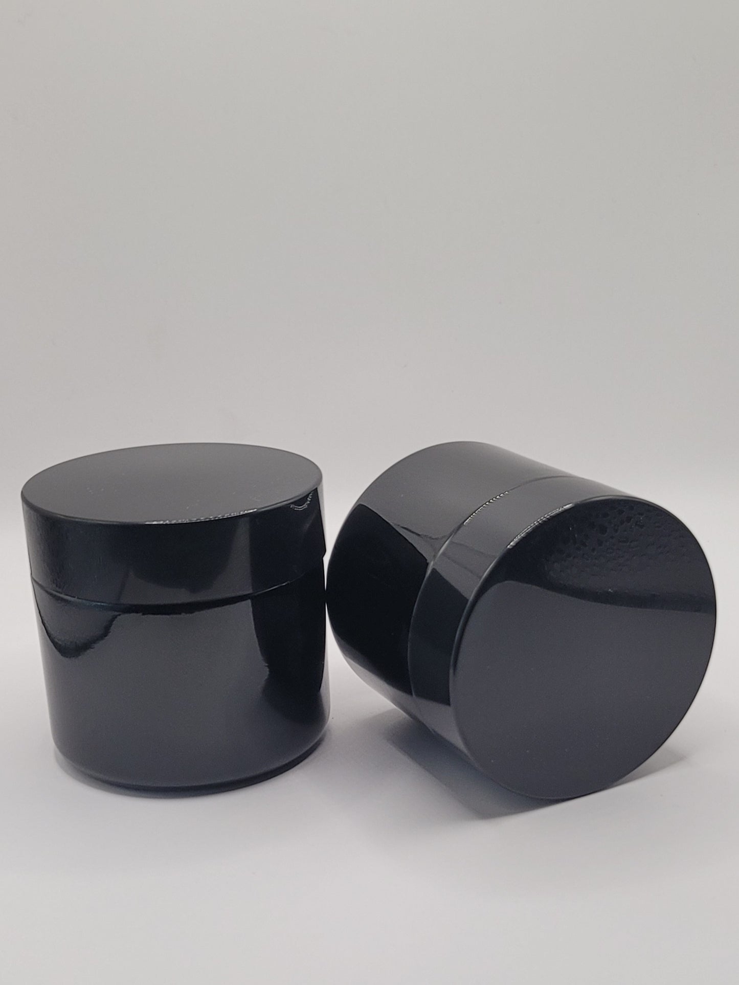 Two black cylindrical containers with lids on a gray background on sitting upright and the other laying down