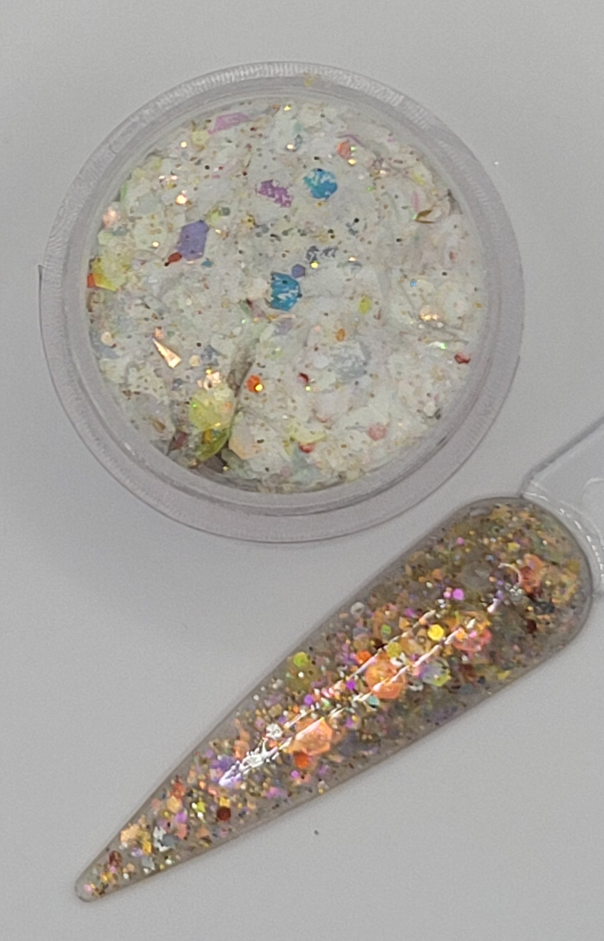 top view glow in the dark Iridescent glitter acrylic in a jar next to a swatchstick against a light gray background