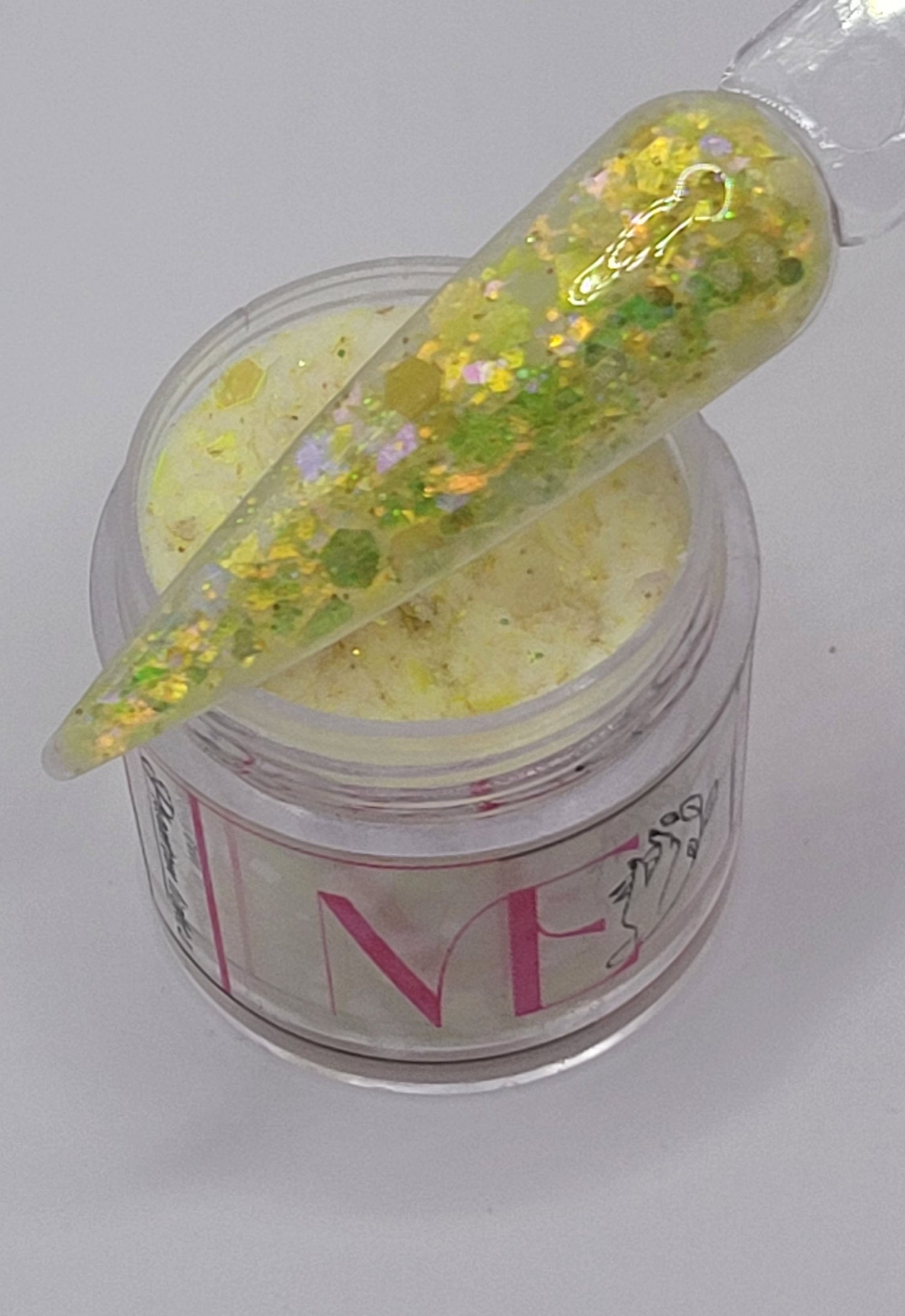 yellow glow in the dark Iridescent glitter acrylic in a jar with a swatchstick over top against a light gray background