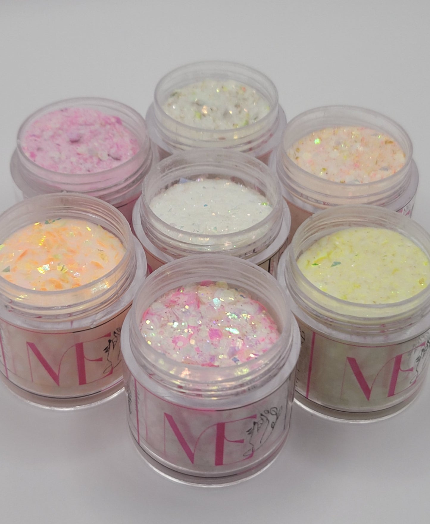 seven Jars of glitter acrylic with visible ME brand name on a white background