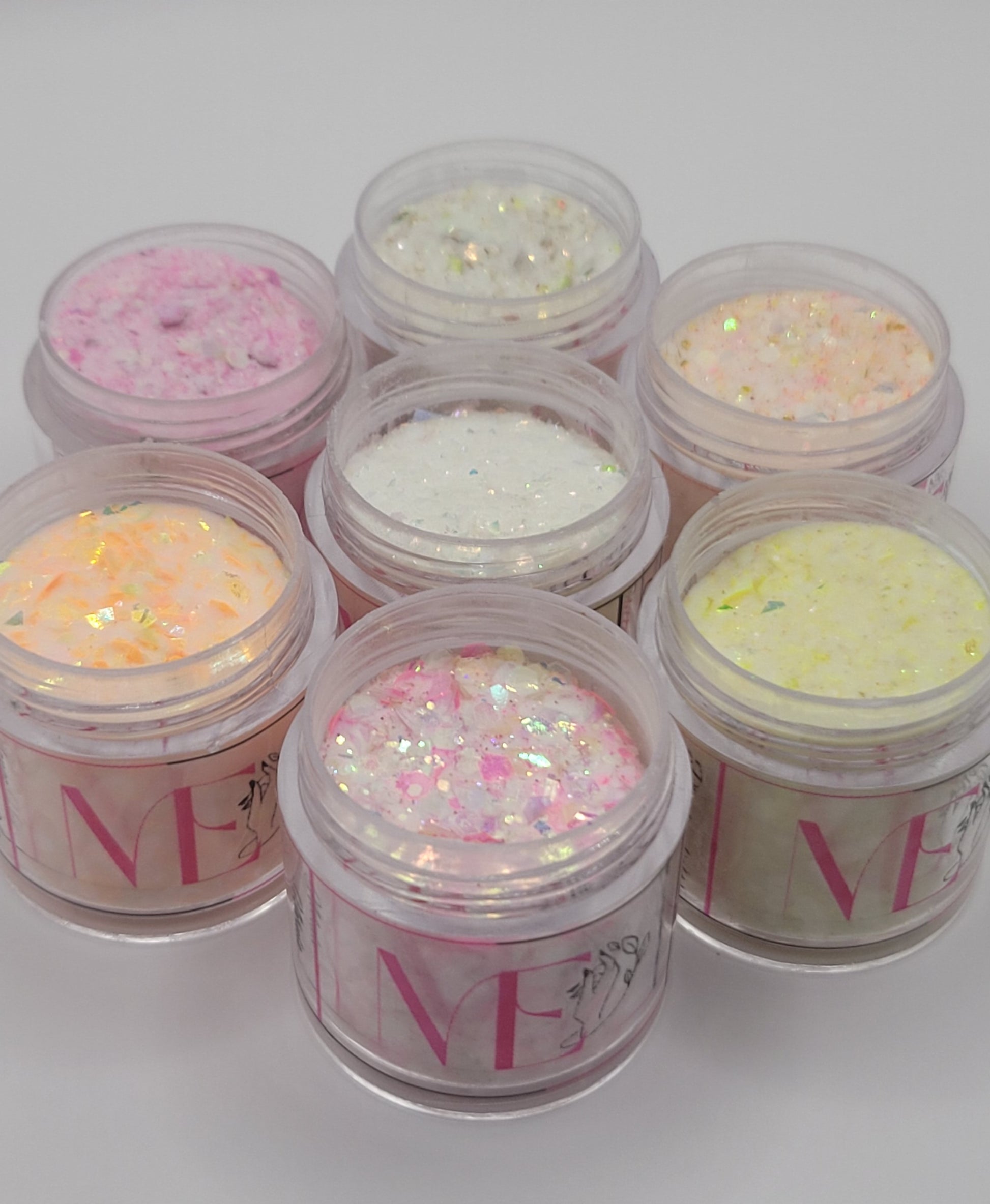 seven Jars of glitter acrylic with visible ME brand name on a white background