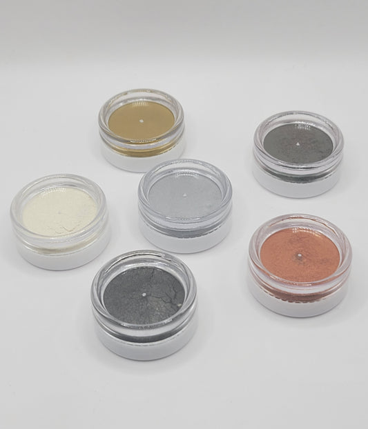 Six small containers upside down with different metallic mica powders on a white background
