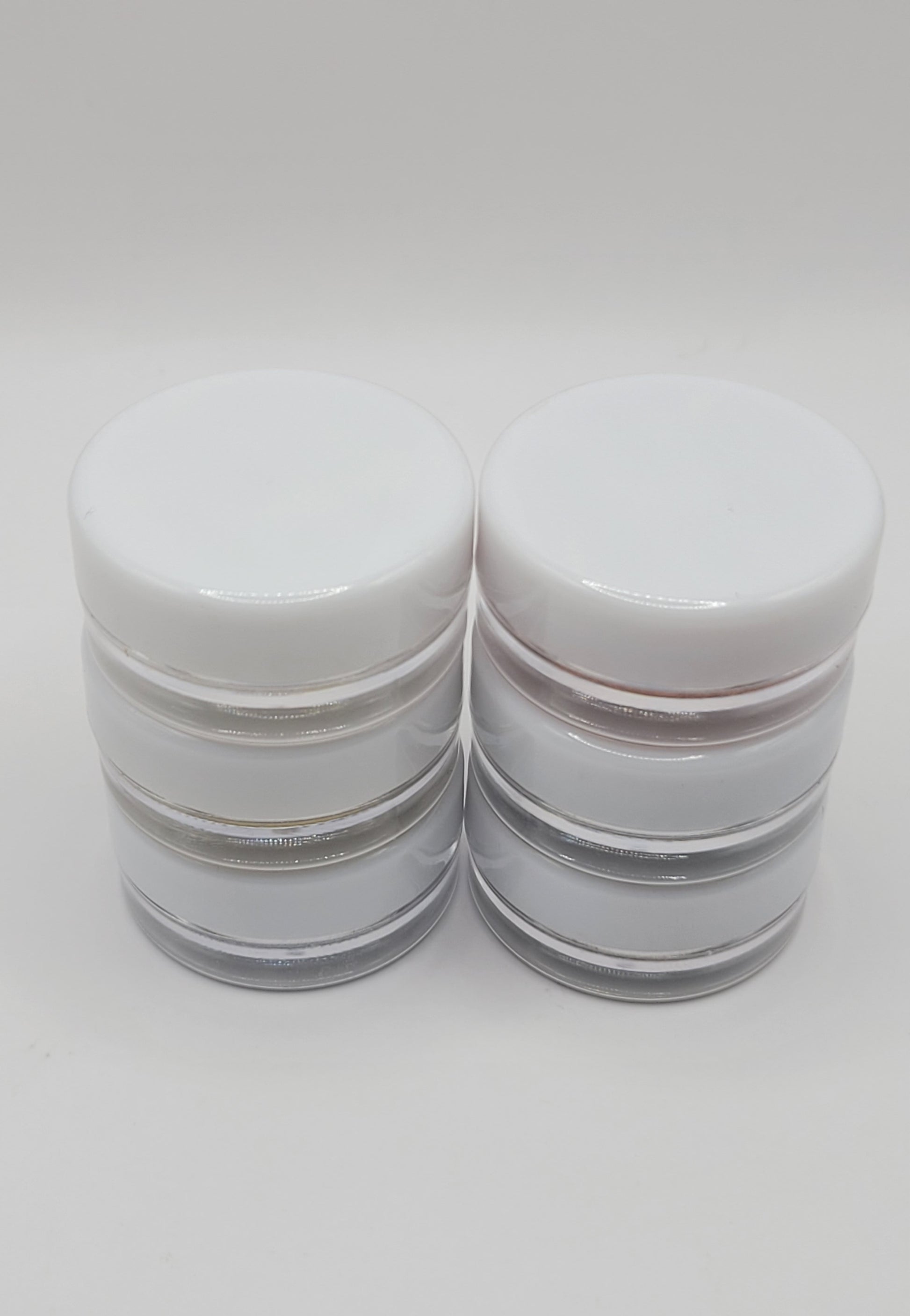 six cosmetic jars with white lids stacked in two sets on a light gray background